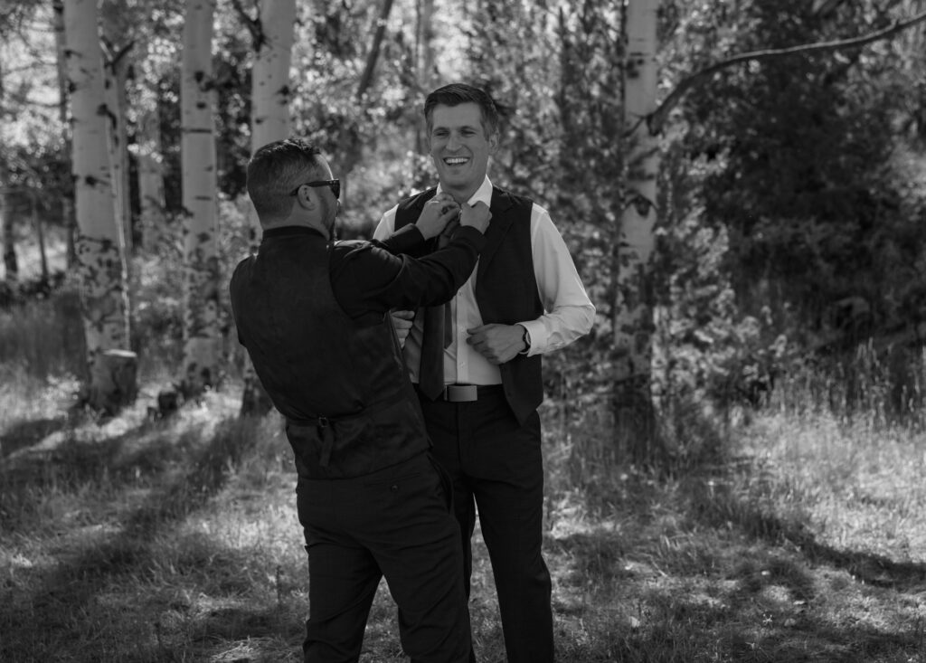 groomsman helping groom get ready for a wedding in the fall in colorado